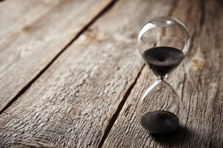 Hourglass on wooden background, closeup. Urgency and running out of time concept
